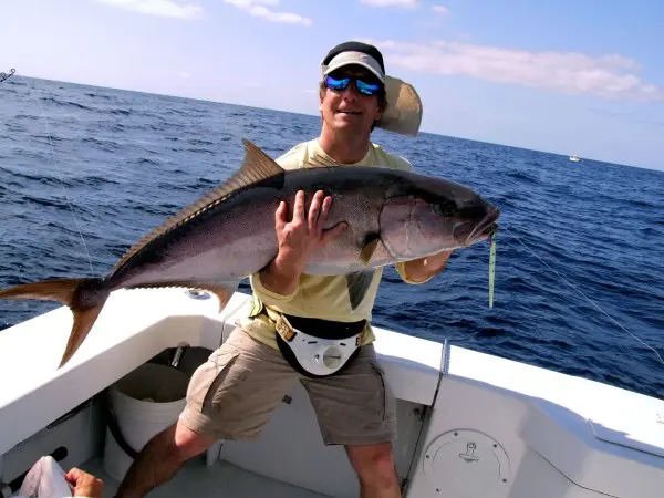 A man holding a fish while standing on top of a boat.